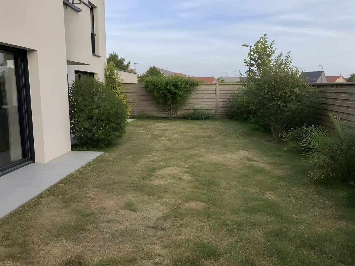Pelouse jaunie par endroits d'une maison récente, terrasse en dalles grises