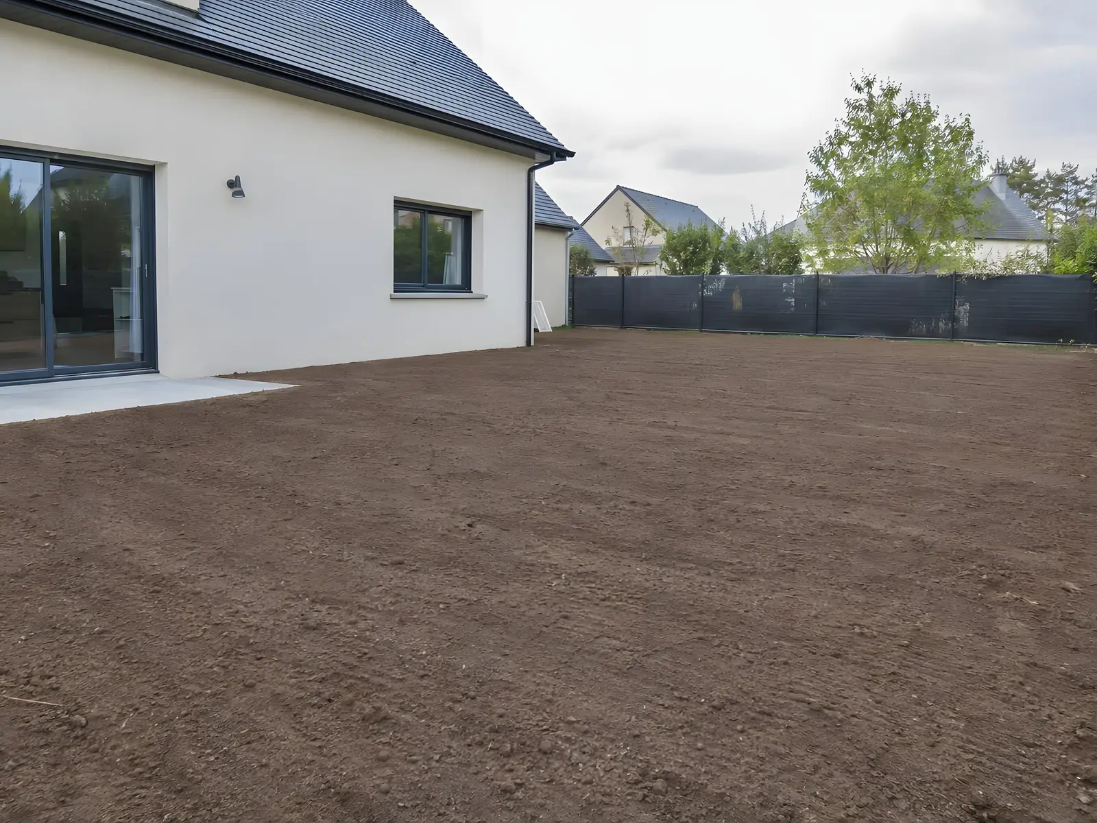 Terrain derrière une maison neuve aux murs blancs remis à plat, terre brune ratissée sans une souche ni une ronce