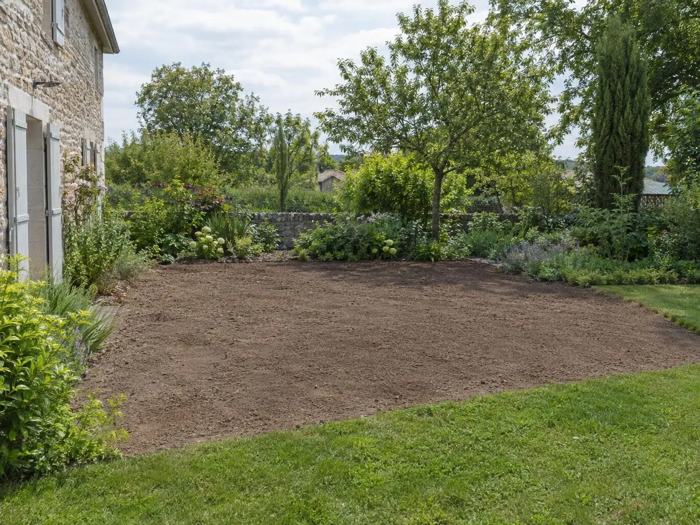 Terre végétale brune finement ratissée à la place de la dalle, près de la maison en pierre, prête à semer