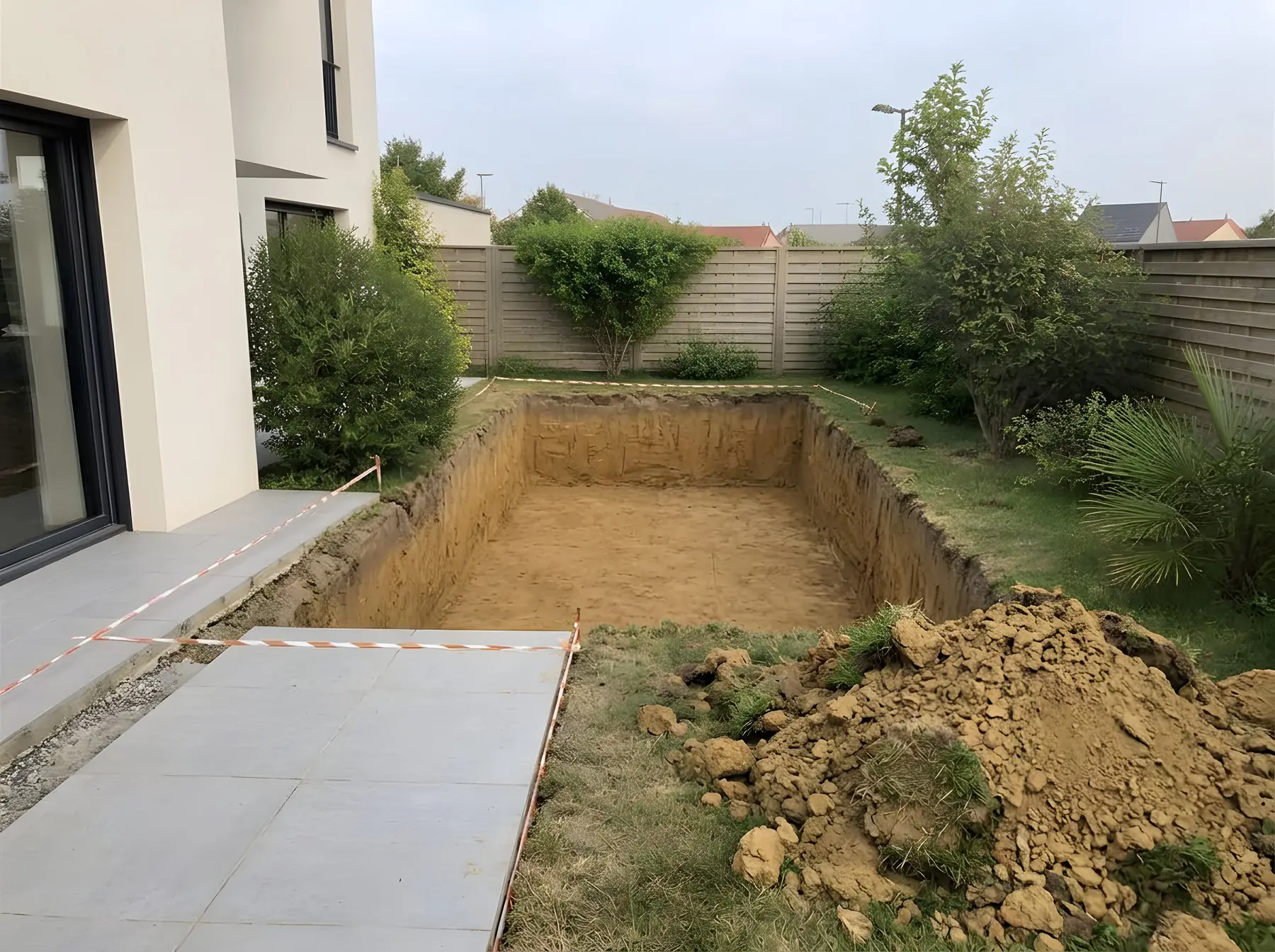 La même pelouse ouverte d'une fouille de piscine rectangulaire au bout de la terrasse, terre en tas devant