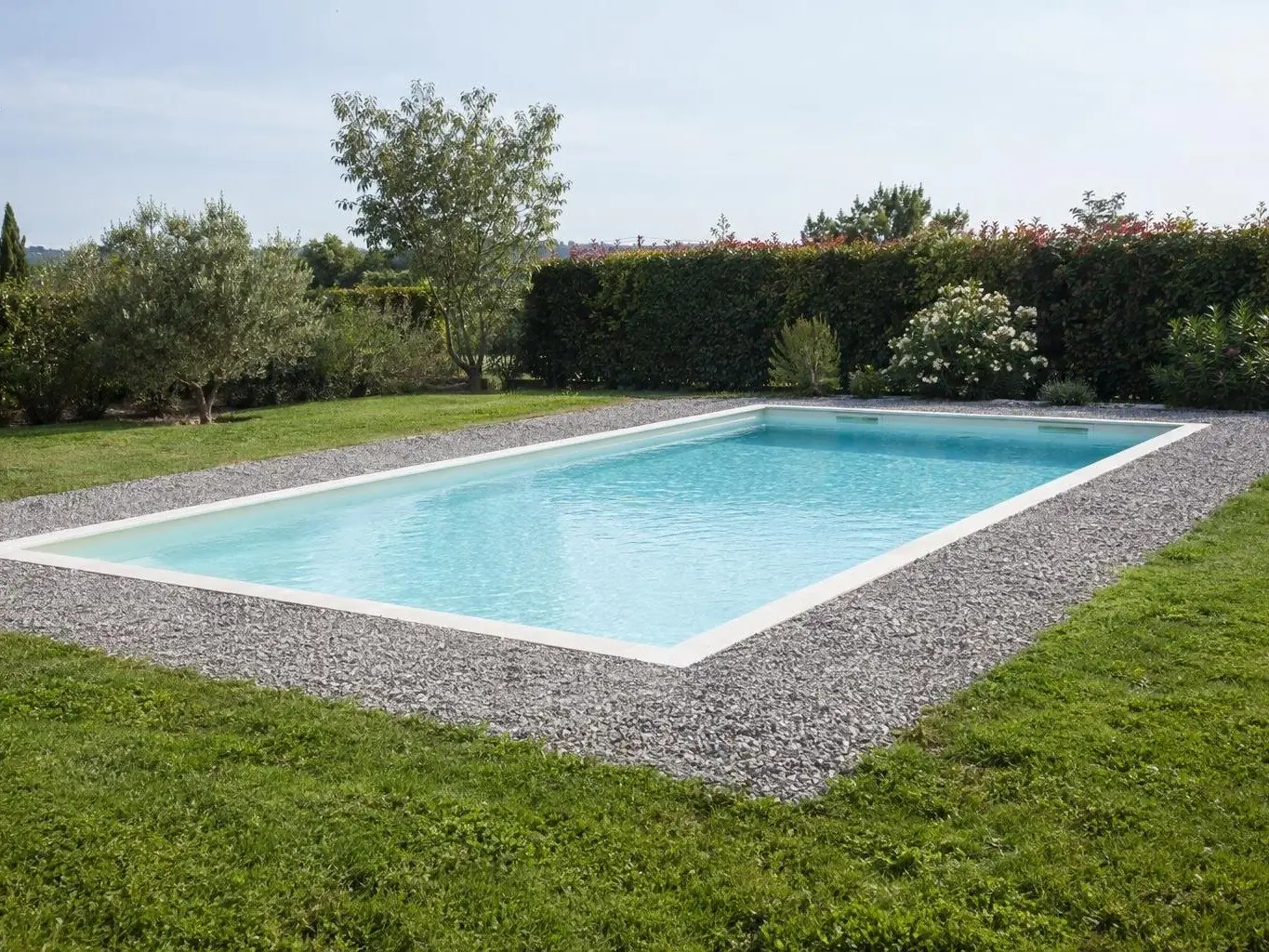 Piscine coque remplie d'eau claire entourée d'une bande de gravier gris à niveau, pelouse tout autour