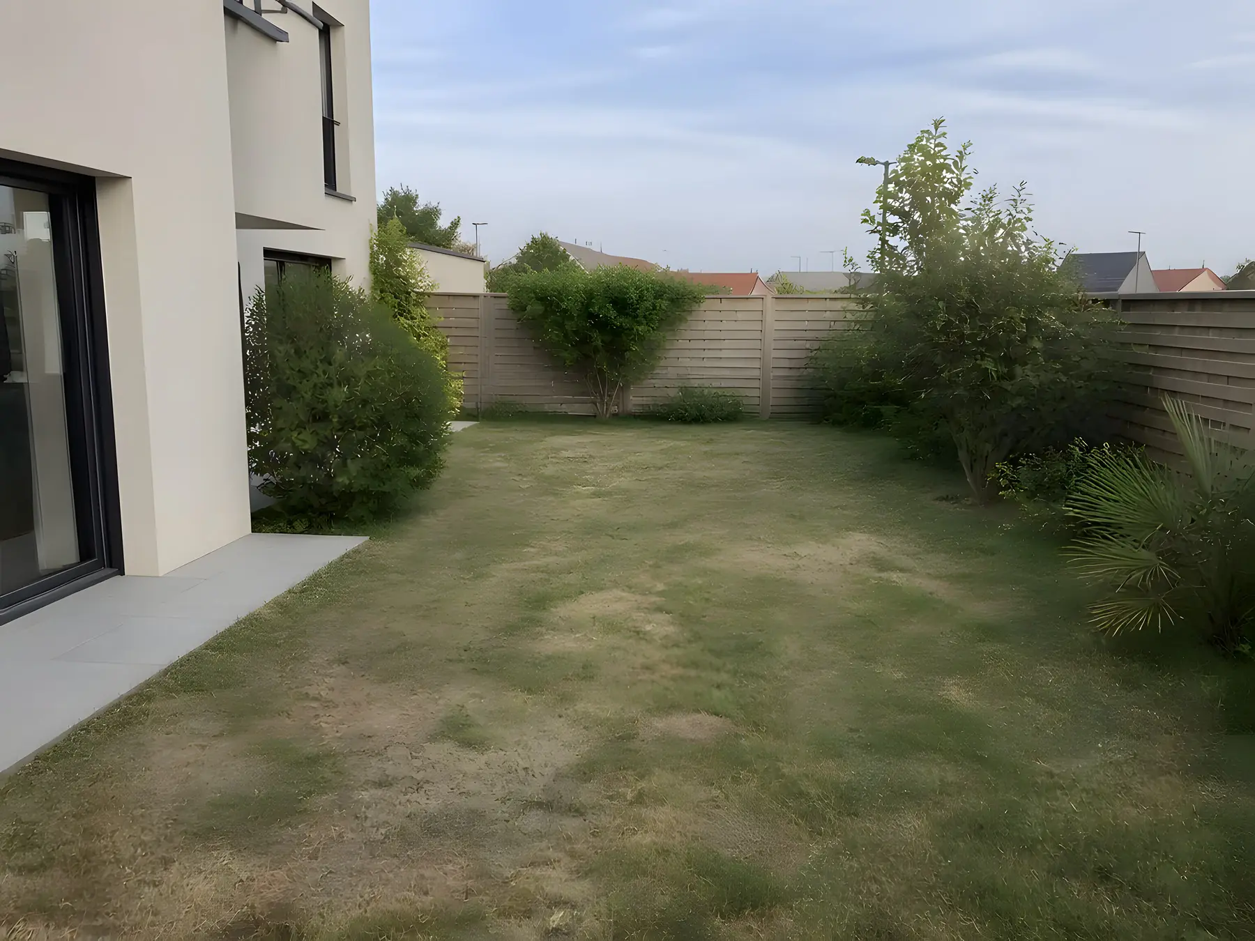 Pelouse d'une maison récente au bout de sa terrasse en dalles grises, là où la piscine sera creusée
